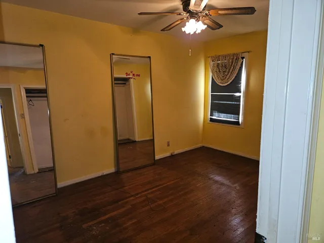 an empty room with wooden floor closet and windows