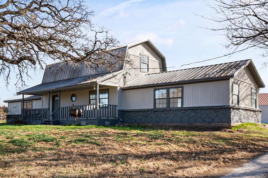 443 County Road 3799 Springtown, TX 76082 - Photo 2 of 33 View of front facade with a porch, a metal roof, stone siding, and a front lawn