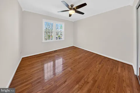an empty room with wooden floor ceiling fan and windows
