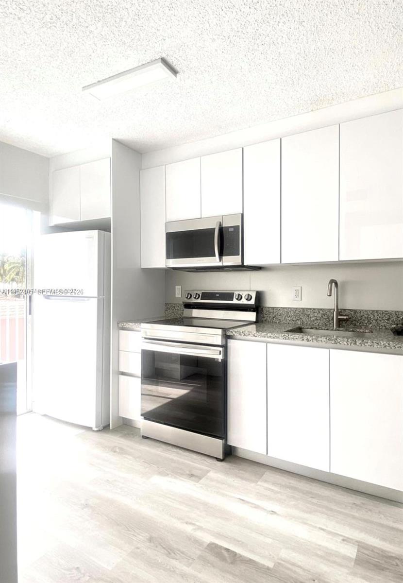 2575 Southwest 27th Avenue, Unit 210 Miami, FL 33133 - Photo 4 of 16 a kitchen with granite countertop a stove a sink and a microwave