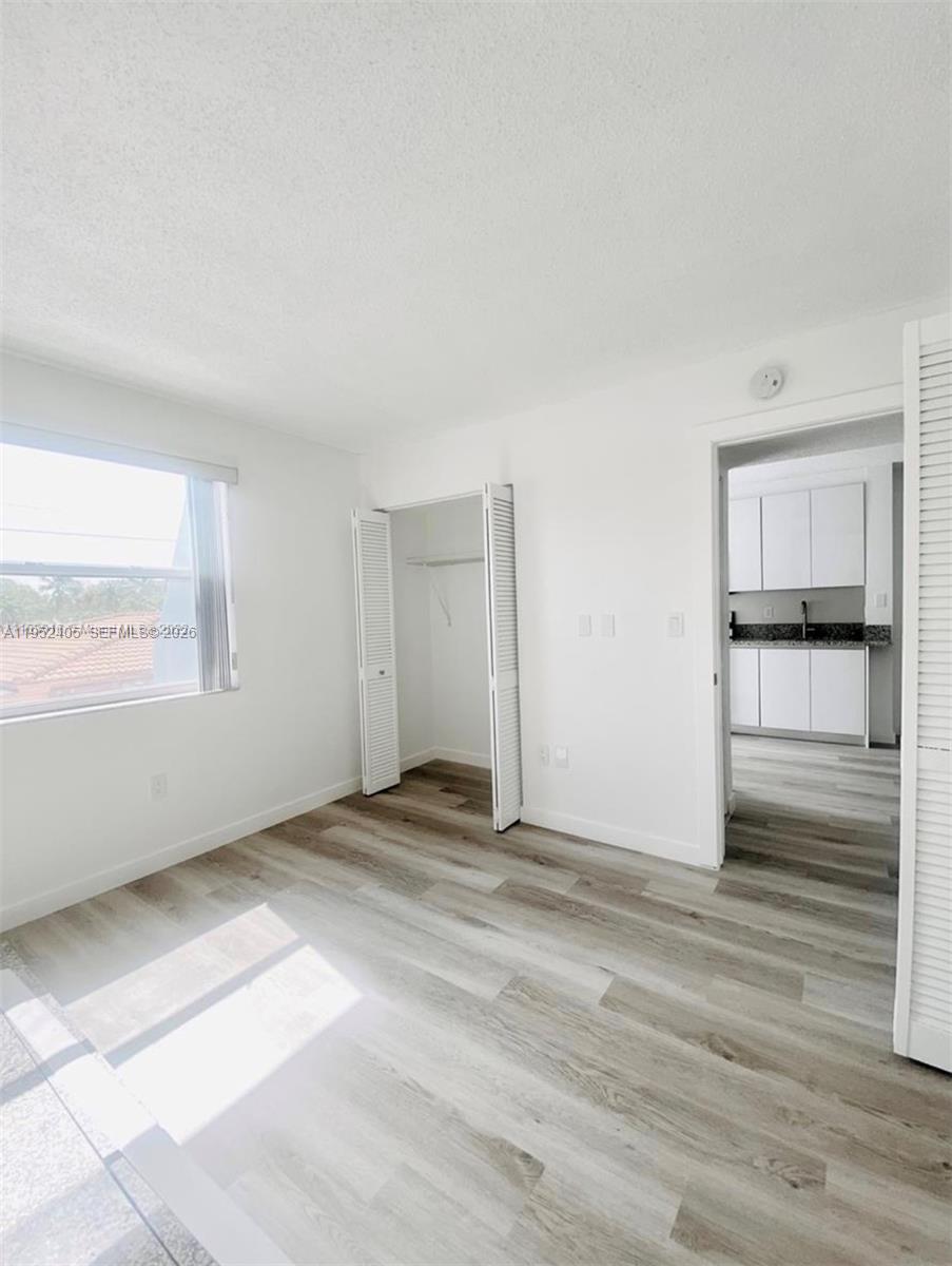 2575 Southwest 27th Avenue, Unit 210 Miami, FL 33133 - Photo 9 of 16 a view of an empty room with wooden floor and a kitchen