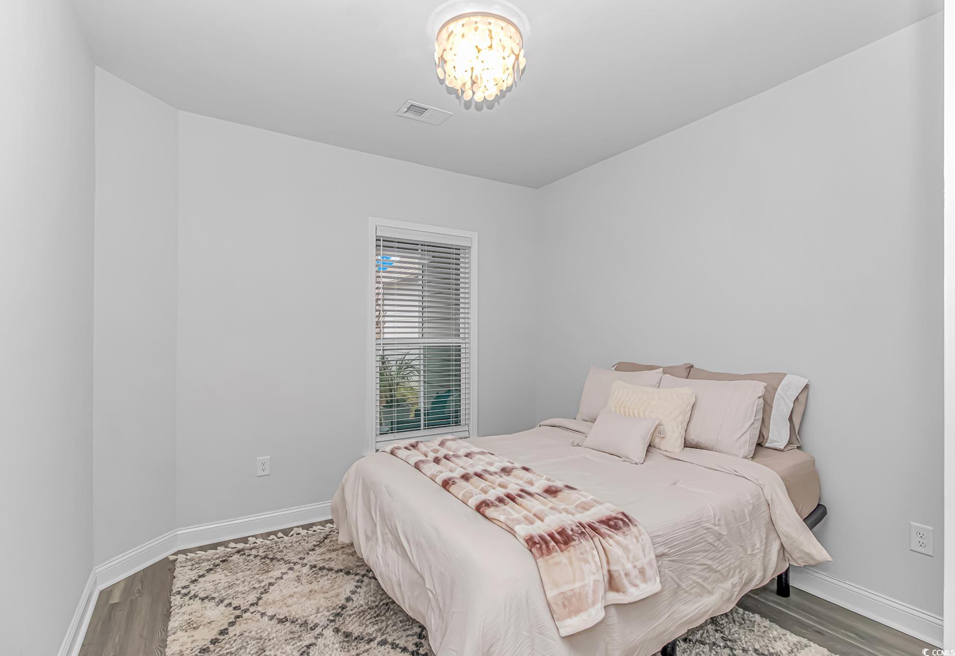 6076 Campanella Street Myrtle Beach, SC 29577 - Photo 19 of 29 Bedroom featuring visible vents, wood finished floors, baseboards, and a notable chandelier