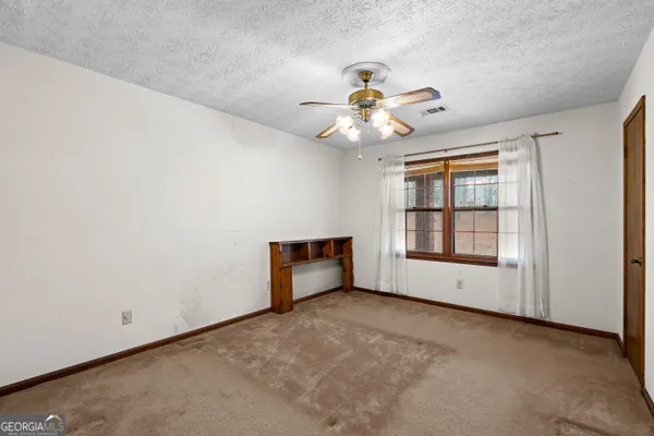 an empty room with chandelier fan and windows