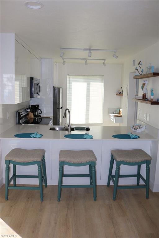 2235 San Marco Road, Unit 5204 Marco Island, FL 34145 - Photo 7 of 34 Kitchen featuring a peninsula with seating, a stainless steel sink with a high-arc faucet, and light-toned wood-finish flooring