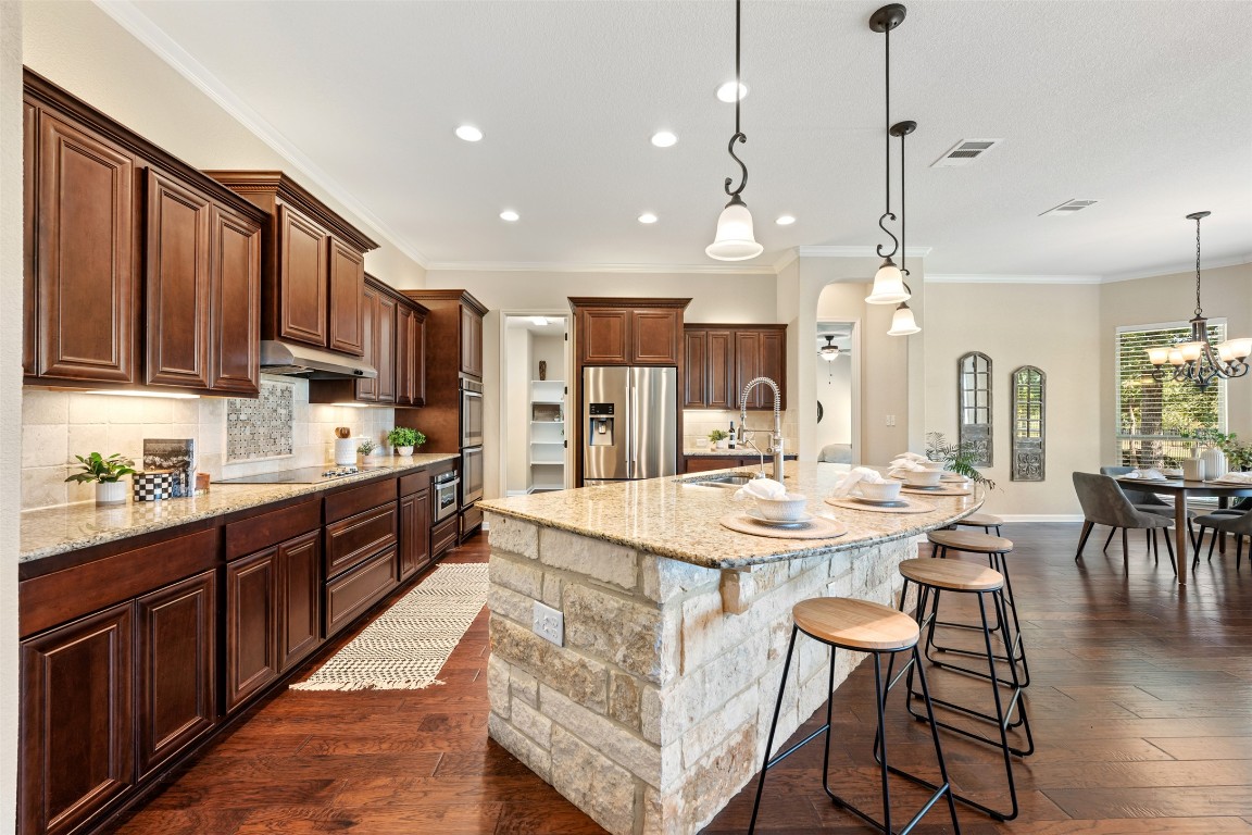129 Camp Verde Drive Georgetown, TX 78633 - Photo 12 of 39 Kitchen featuring a kitchen breakfast bar, decorative backsplash, crown molding, light stone countertops, and hanging light fixtures