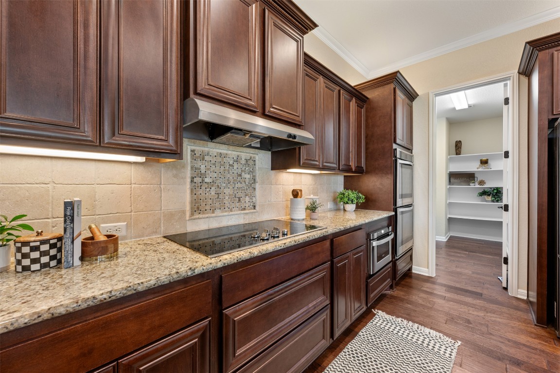 129 Camp Verde Drive Georgetown, TX 78633 - Photo 13 of 39 Kitchen with ornamental molding, light stone countertops, dark brown cabinetry, decorative backsplash, and dark wood-style flooring