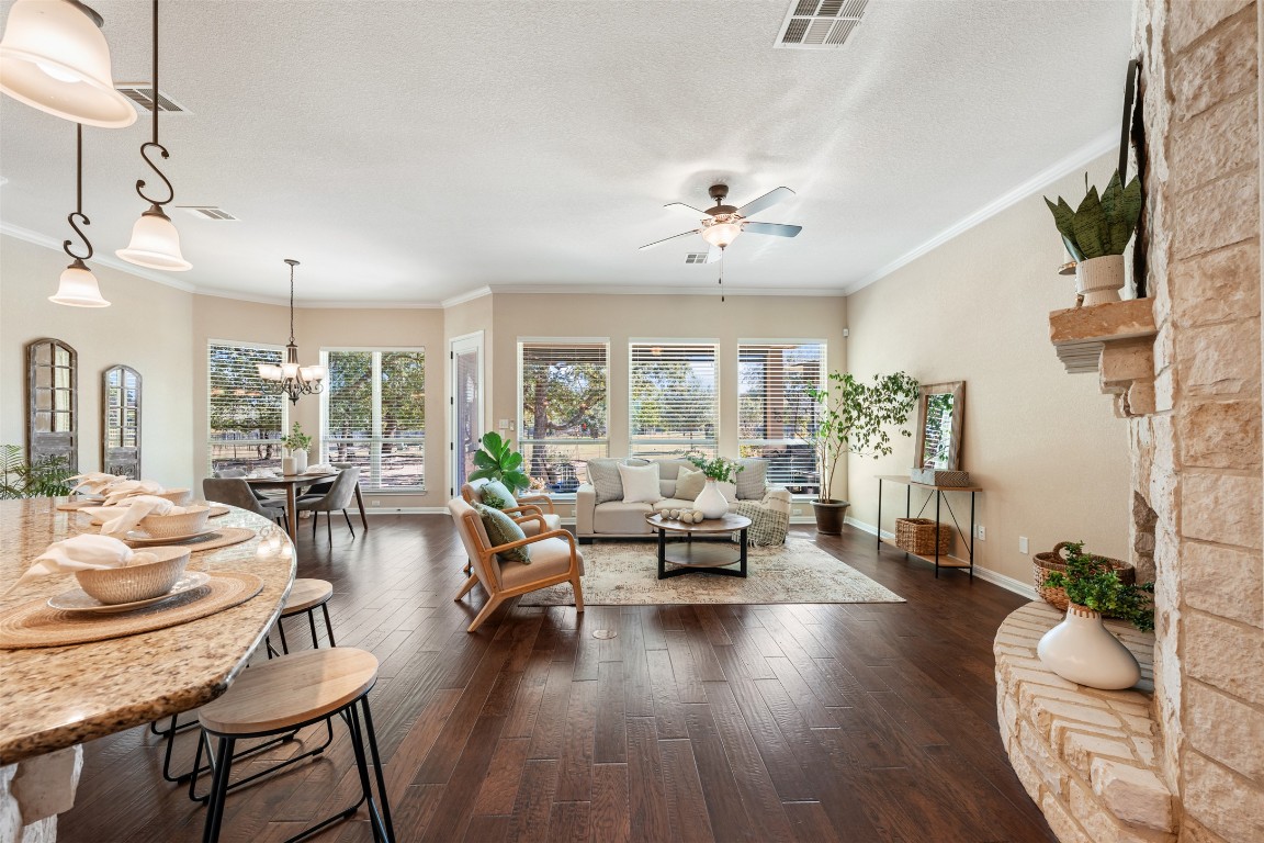 129 Camp Verde Drive Georgetown, TX 78633 - Photo 14 of 39 Living area with dark wood-style flooring, a stone fireplace, healthy amount of natural light, crown molding, and a chandelier