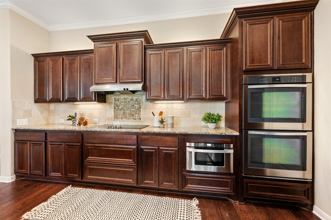 129 Camp Verde Drive Georgetown, TX 78633 - Photo 15 of 39 Kitchen featuring stainless steel double oven, light stone countertops, backsplash, ornamental molding, and dark wood-style flooring