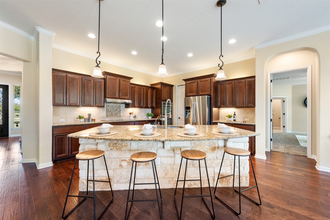 129 Camp Verde Drive Georgetown, TX 78633 - Photo 16 of 39 Kitchen with tasteful backsplash, a kitchen bar, dark wood-style flooring, ornamental molding, and light stone counters