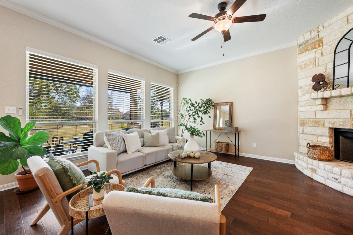 129 Camp Verde Drive Georgetown, TX 78633 - Photo 18 of 39 Living room with dark wood-style floors, crown molding, a stone fireplace, and a ceiling fan