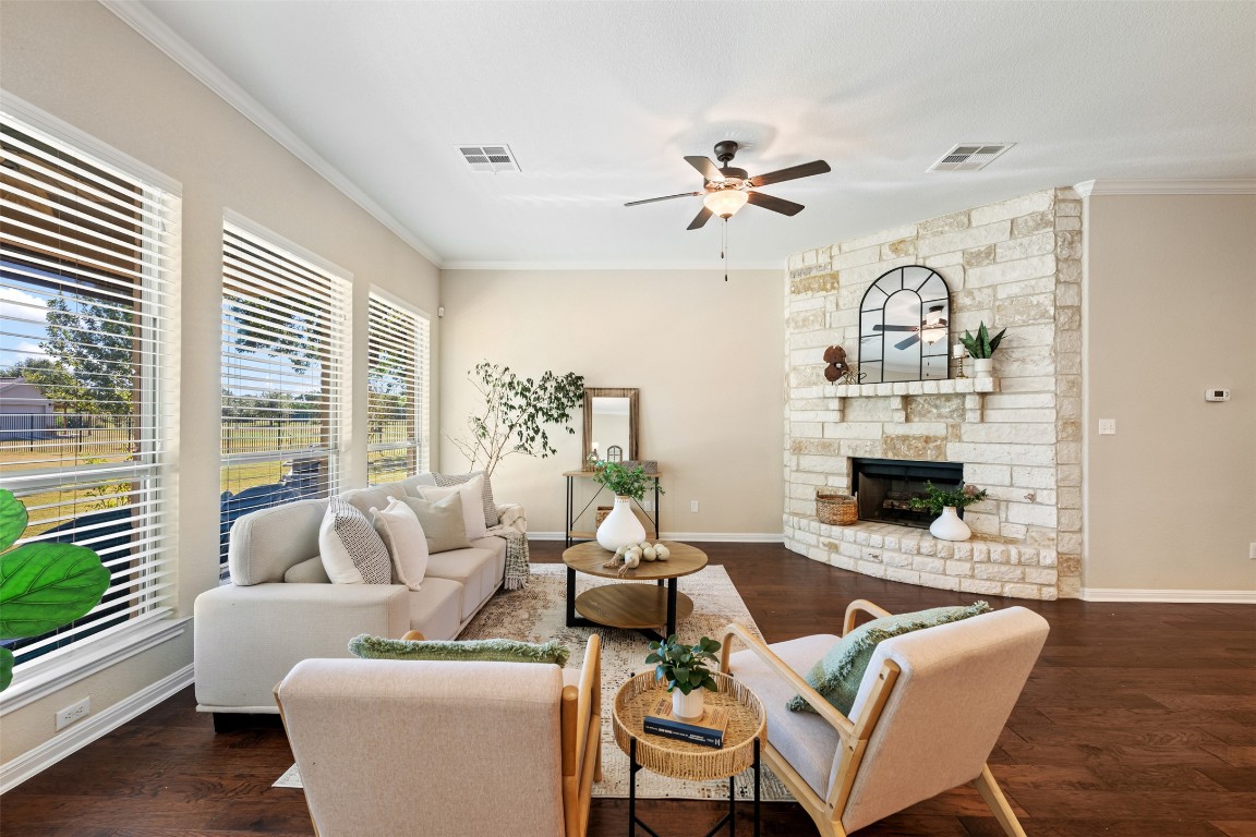 129 Camp Verde Drive Georgetown, TX 78633 - Photo 19 of 39 Living area with ornamental molding, dark wood-type flooring, a ceiling fan, and a stone fireplace