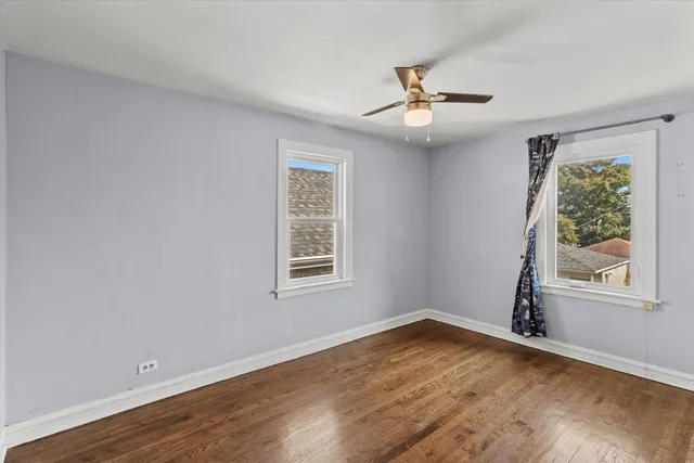 an empty room with wooden floor chandelier fan and windows