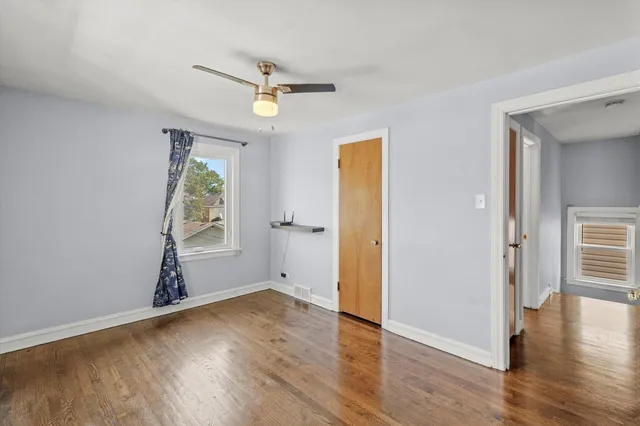 an empty room with wooden floor a ceiling fan and windows