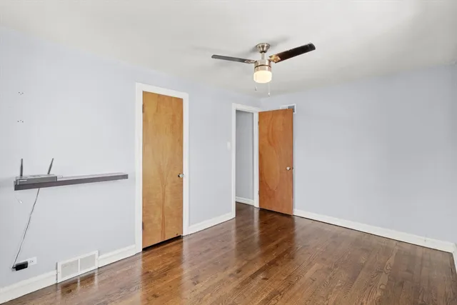 a view of an empty room with wooden floor and a ceiling fan