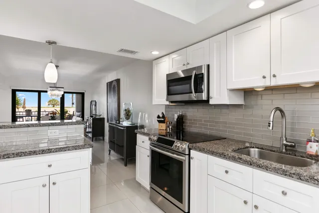 a kitchen with granite countertop white cabinets sink and stainless steel appliances