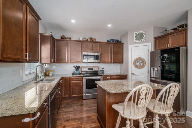 a kitchen with stainless steel appliances granite countertop a sink a stove a refrigerator cabinets and a dining table