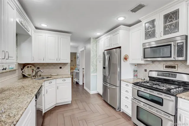 a kitchen with stainless steel appliances granite countertop a stove top oven a refrigerator and white cabinets with wooden floor