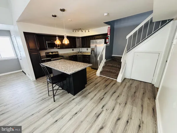 a living room with stainless steel appliances wooden floors and kitchen view