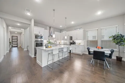 a kitchen with stainless steel appliances kitchen island granite countertop a stove a refrigerator a kitchen island a dining table and chairs with wooden floor