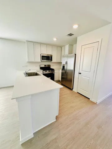 a kitchen with granite countertop a sink a stove top oven a refrigerator a window and white cabinets