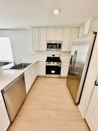 a kitchen with granite countertop a sink a stove top oven a refrigerator a window and white cabinets