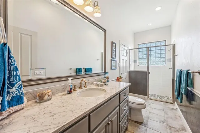 a bathroom with a granite countertop sink a toilet a mirror and shower