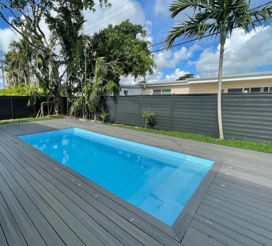 a view of a white house with a swimming pool and lawn chairs under an umbrella