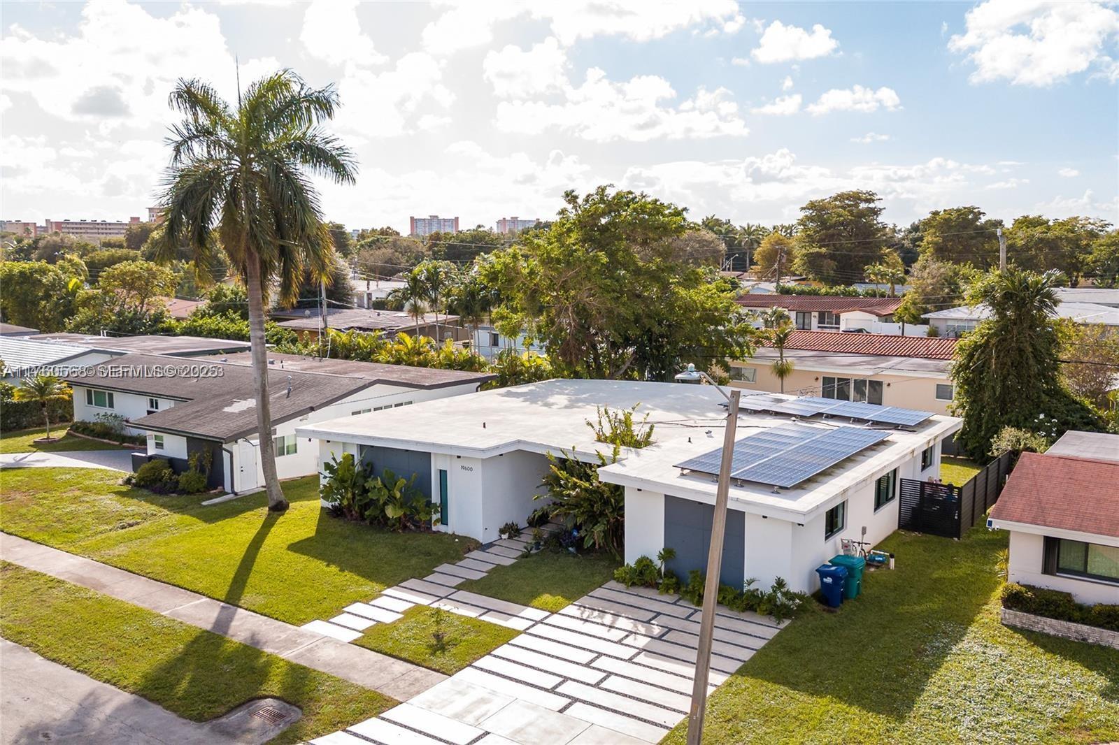 19600 Northeast 19th Avenue Miami, FL 33179 - Photo 32 of 33 a view of a white house with a swimming pool and lawn chairs under an umbrella