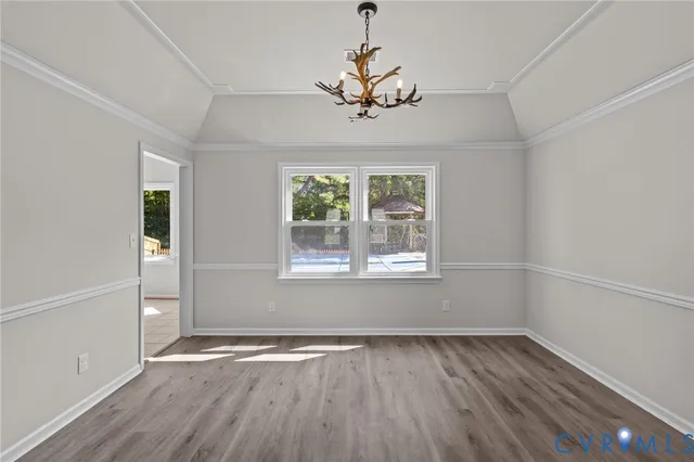 an empty room with wooden floor chandelier and windows