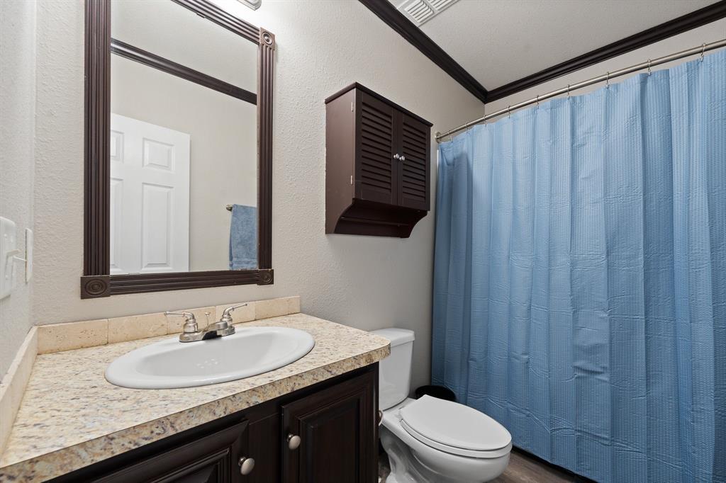 9419 Hilltop Street Rio Vista, TX 76093 - Photo 28 of 40 a bathroom with a granite countertop sink toilet a mirror and shower curtain