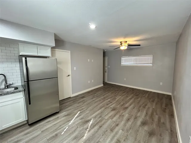 a view of a refrigerator in kitchen and an empty room with wooden floor