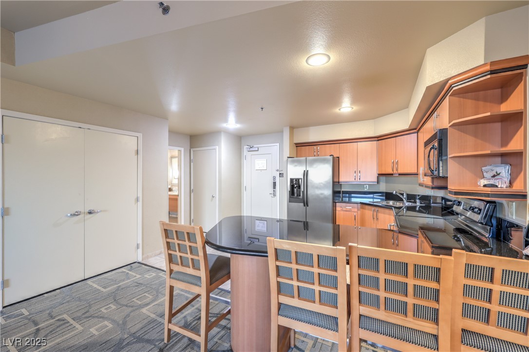 211 East Flamingo Road, Unit 1508 Las Vegas, NV 89169 - Photo 11 of 40 Kitchen featuring open shelves, stainless steel fridge with ice dispenser, black microwave, dark carpet, and a peninsula