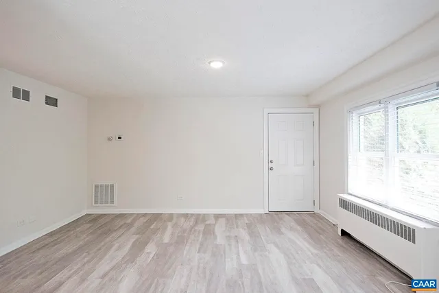 a view of an empty room with wooden floor and a window