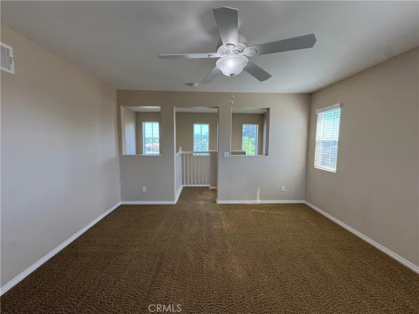 an empty room with a chandelier fan and windows