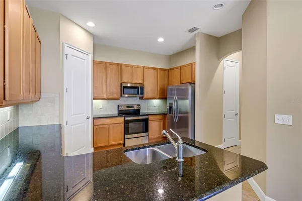 a kitchen with stainless steel appliances granite countertop a refrigerator a stove and a sink with wooden cabinets