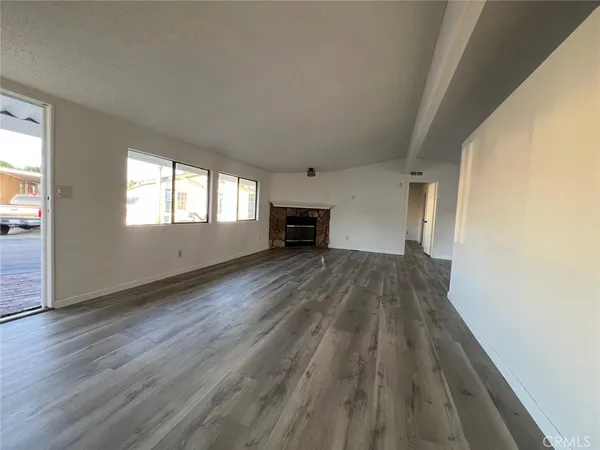 an empty room with wooden floor fireplace and windows