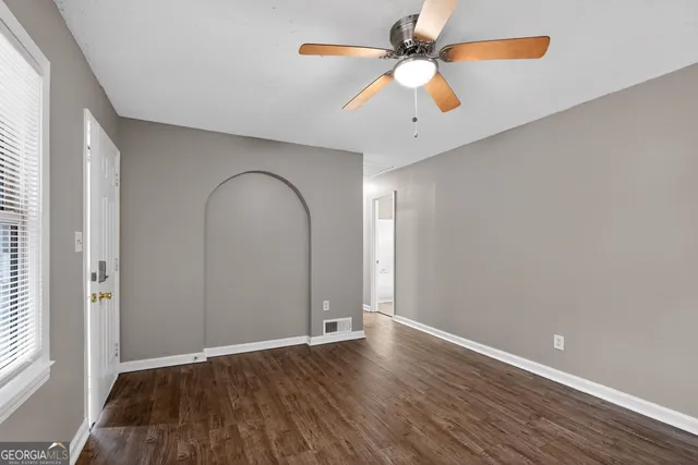 an empty room with wooden floor a ceiling fan and windows