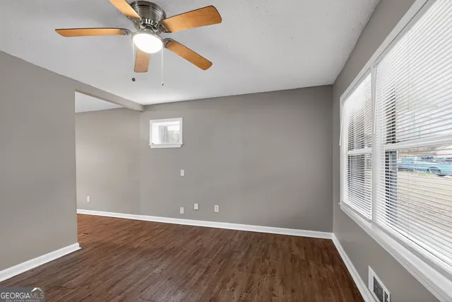 an empty room with wooden floor fan and windows