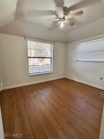 an empty room with wooden floor fan and windows