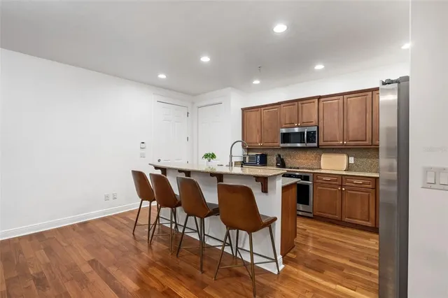 a kitchen with stainless steel appliances granite countertop a stove top oven a sink dishwasher and a chairs with wooden floor