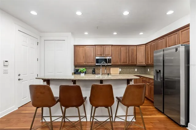 a kitchen with stainless steel appliances granite countertop a refrigerator a sink a stove a dining table and chairs