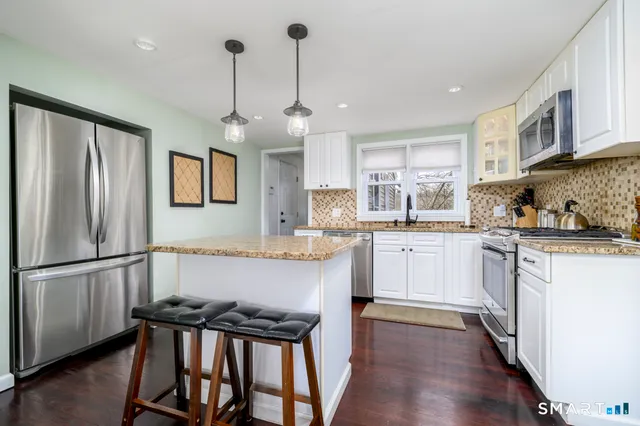 a kitchen with stainless steel appliances granite countertop a refrigerator a sink dishwasher a stove and white cabinets with wooden floor