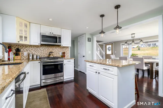 a kitchen with stainless steel appliances white cabinets a sink a stove a microwave and wooden floors