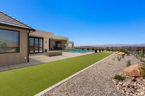 Rear exterior featuring a large patio, built-in pool, artificial turf, and xeriscaped rock garden with mature desert plantings