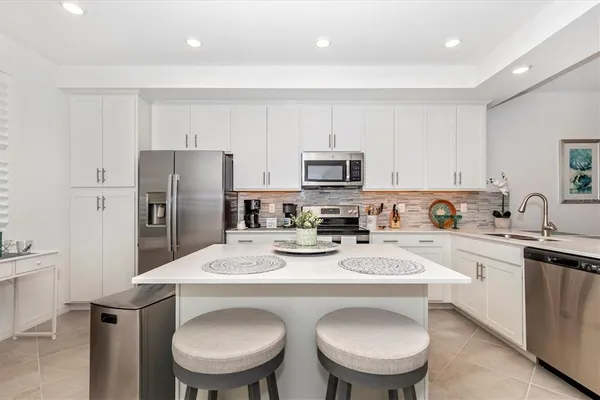 a kitchen with stainless steel appliances granite countertop a sink a stove a refrigerator cabinets and chairs