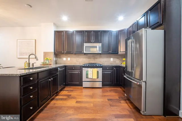 a kitchen with stainless steel appliances kitchen island granite countertop wooden floors wooden cabinets and sink