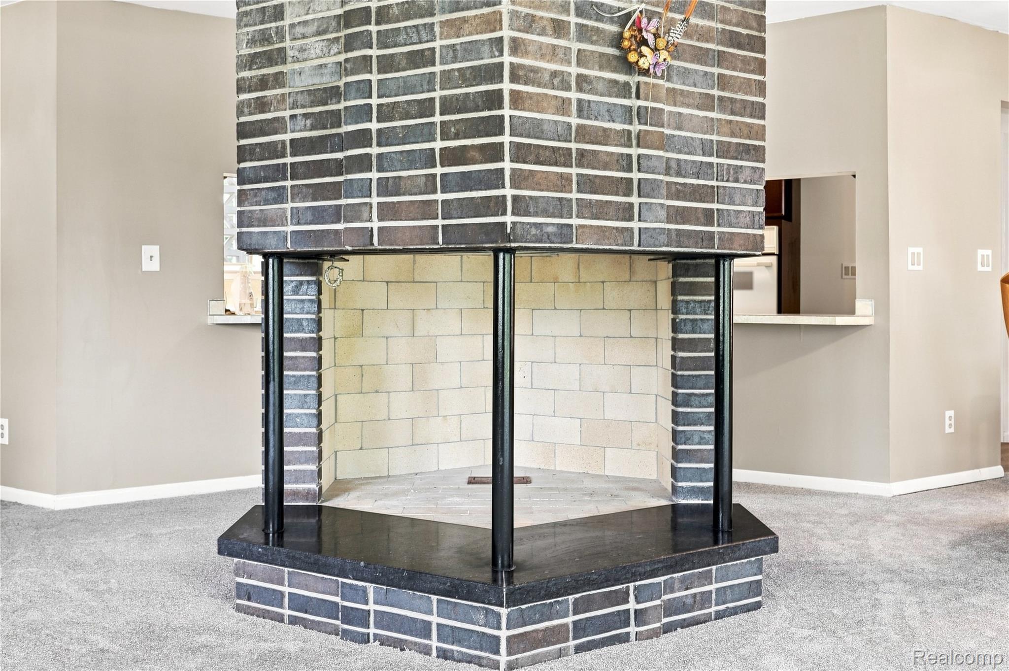 7386 Dean Road Fenton, MI 48430 - Photo 31 of 64 Central brick fireplace with a polished black hearth and three open sides, featuring a white firebox