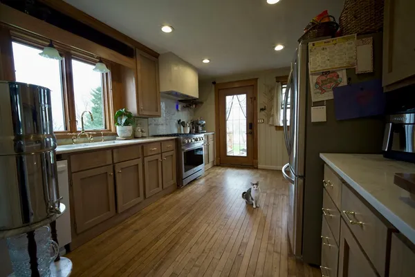 a kitchen with stainless steel appliances granite countertop a refrigerator a sink dishwasher a stove and white countertops with wooden floor