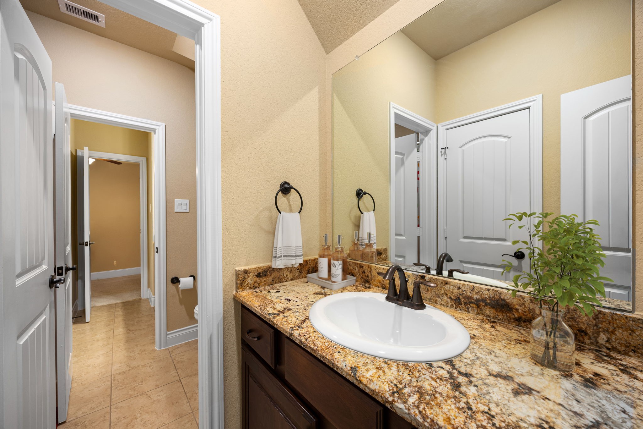 23421 Cannondale Loop Montgomery, TX 77316 - Photo 32 of 47 Stylish and well-appointed bathroom featuring a granite countertop vanity, rich wood cabinetry, and an oversized mirror that enhances light and space. Elegant fixtures and a warm neutral palette create a clean, inviting atmosphere perfect for everyday comfort and guests alike.