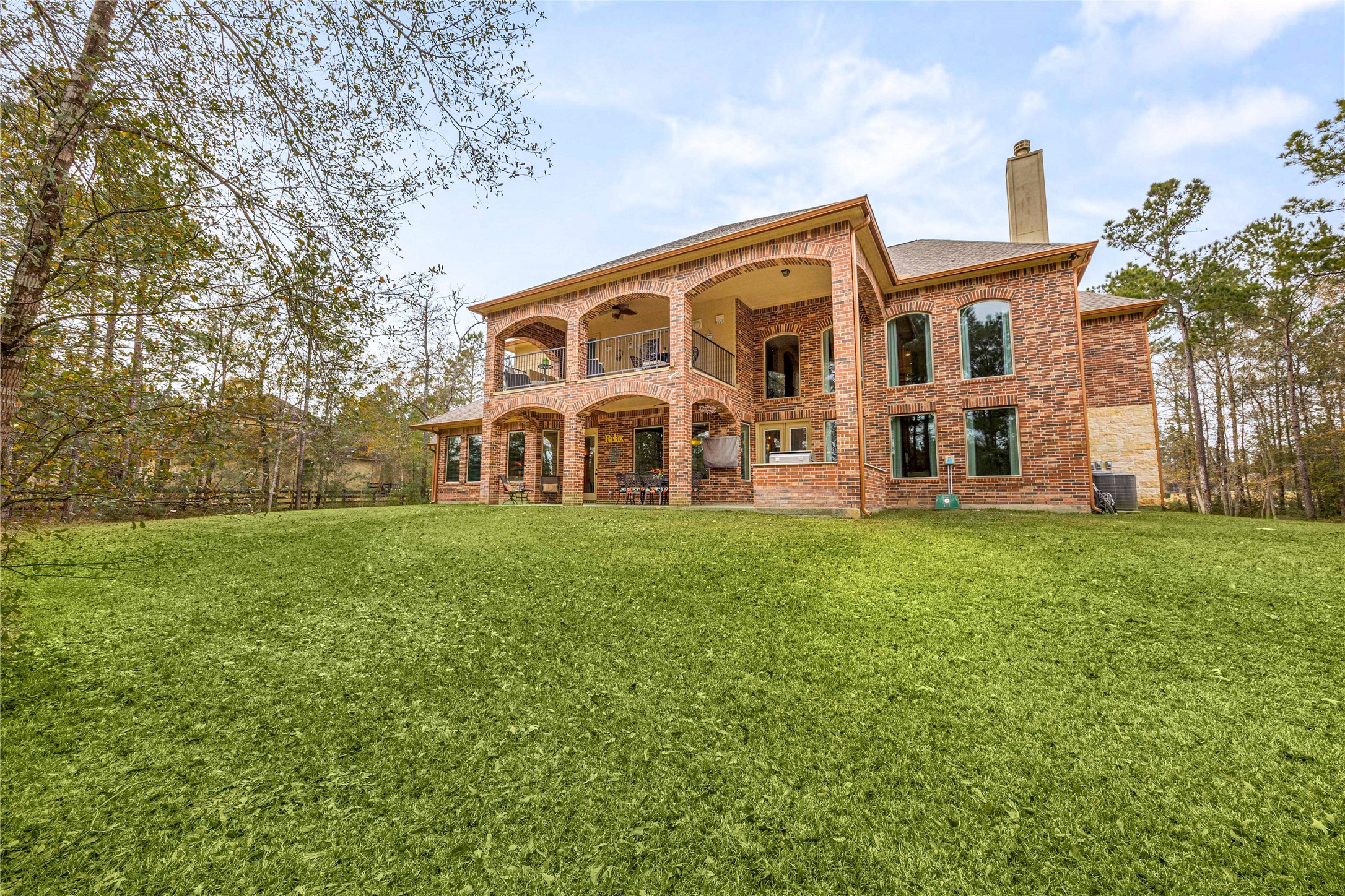 23421 Cannondale Loop Montgomery, TX 77316 - Photo 33 of 47 Expansive backyard with a lush green lawn and a beautiful two-story brick exterior featuring covered patios on both levels. Large windows line the rear of the home, creating seamless indoor-outdoor connection and plenty of natural light. Surrounded by mature trees, this space offers privacy, room to play, and endless potential for outdoor living and entertaining.